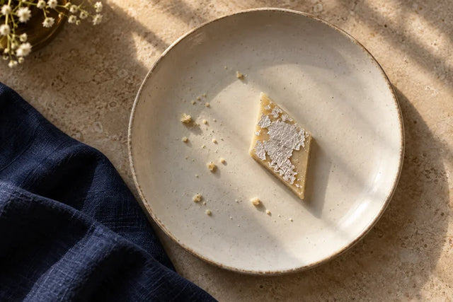 A single silver-topped diamond of kaju katli on an ivory plate.