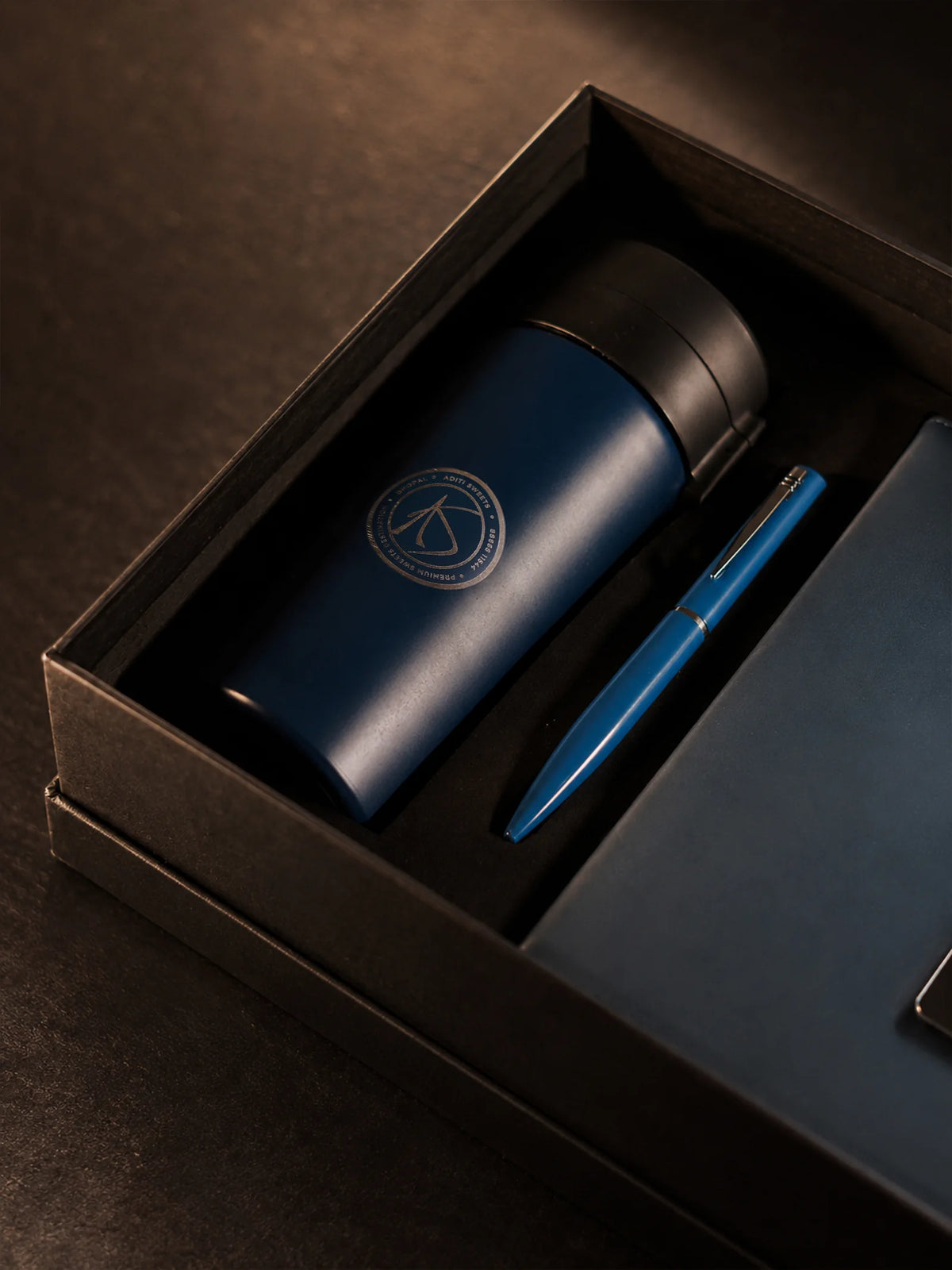 Close-up of a navy tumbler, pen and notebook in a corporate gift box.