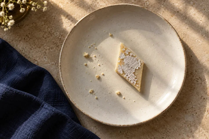 A single silver-topped diamond of kaju katli on an ivory plate.